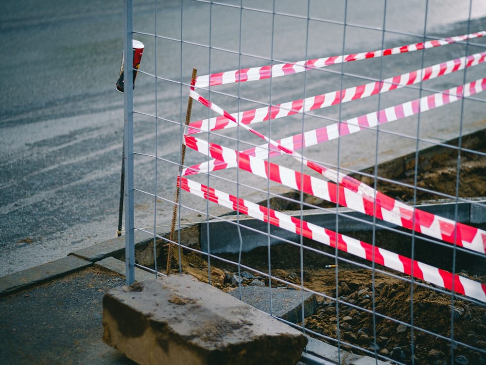 Byggstängsel med rödvit avspärrningstejp framför en schaktgrop